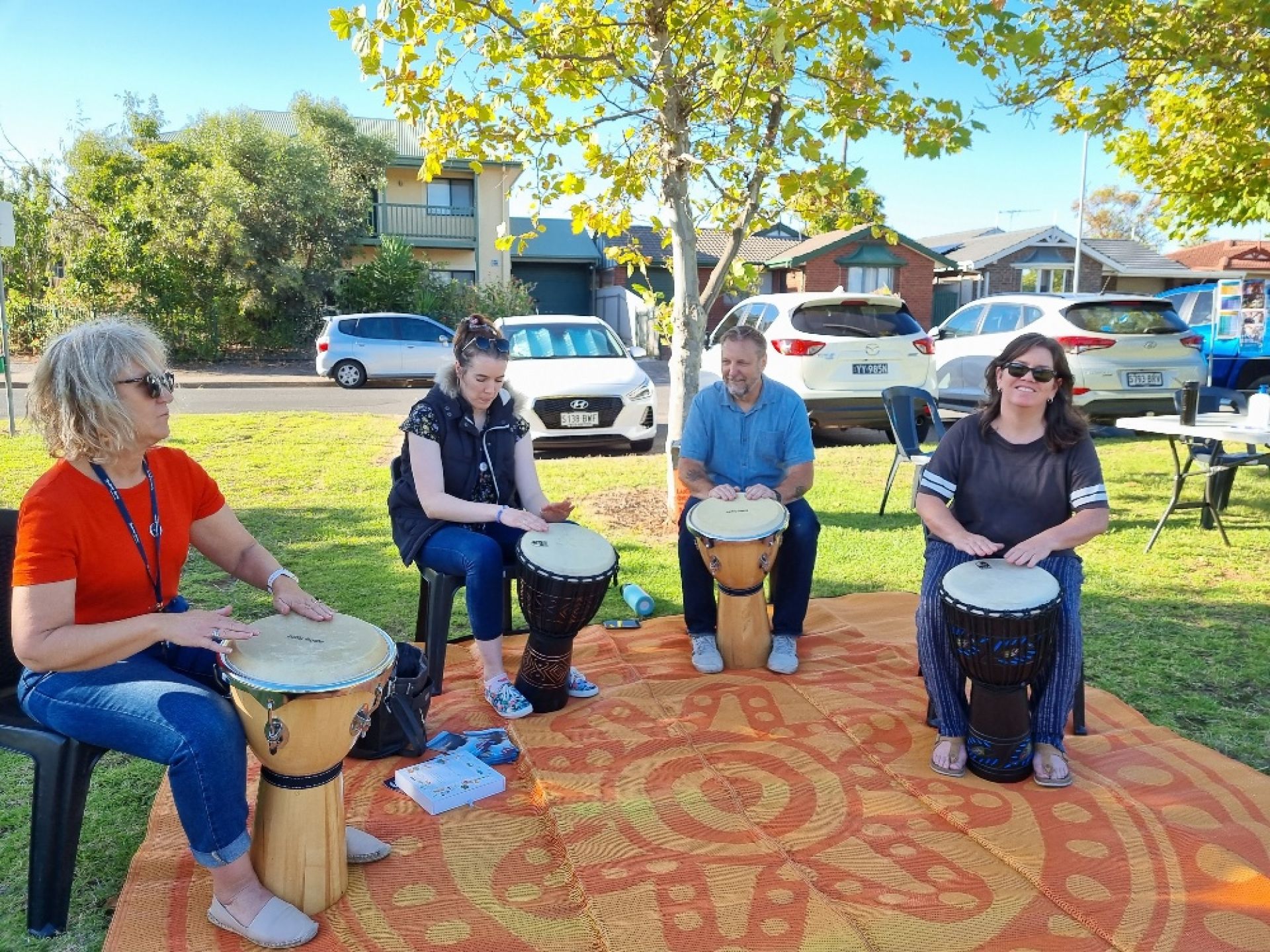 4 adults sitting in a park playing drums
