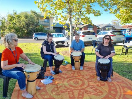 4 adults sitting in a park playing drums