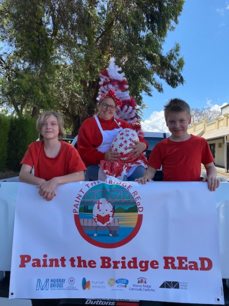 2 children and an adult participating in a pageant with a banner 'Paint the town Read' and the big egg.