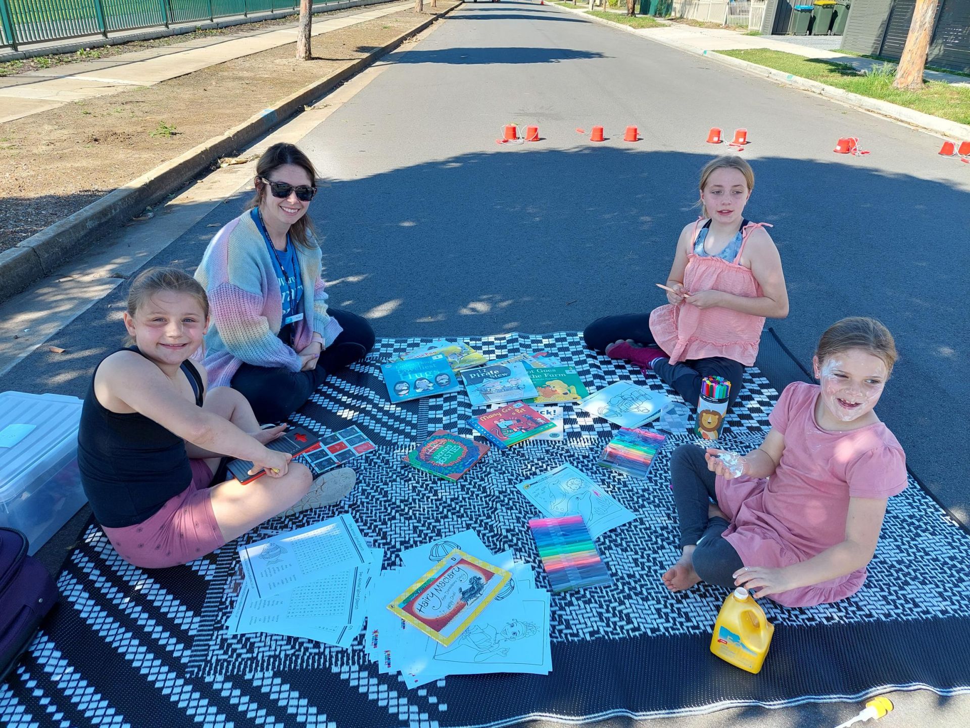 4 people sitting on a rug on a street doing colouring in.