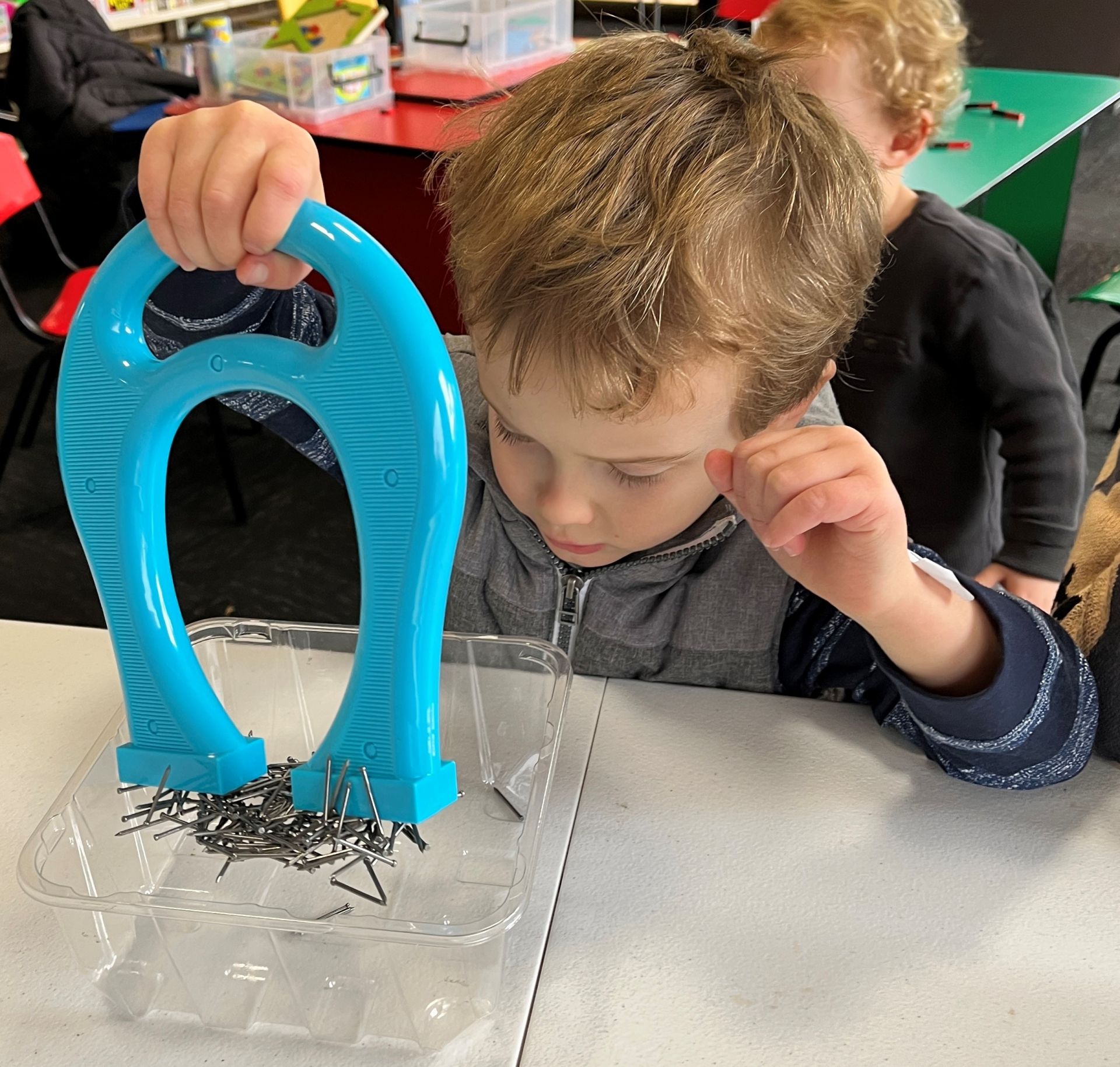 Little boy using a large blue magnet to pick up a collection of small metal objects