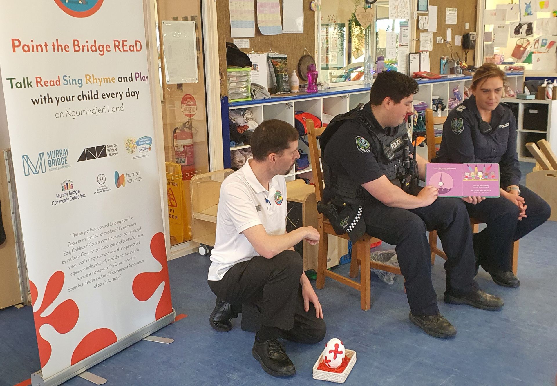 Three adults reading a story at a playgroup centre.