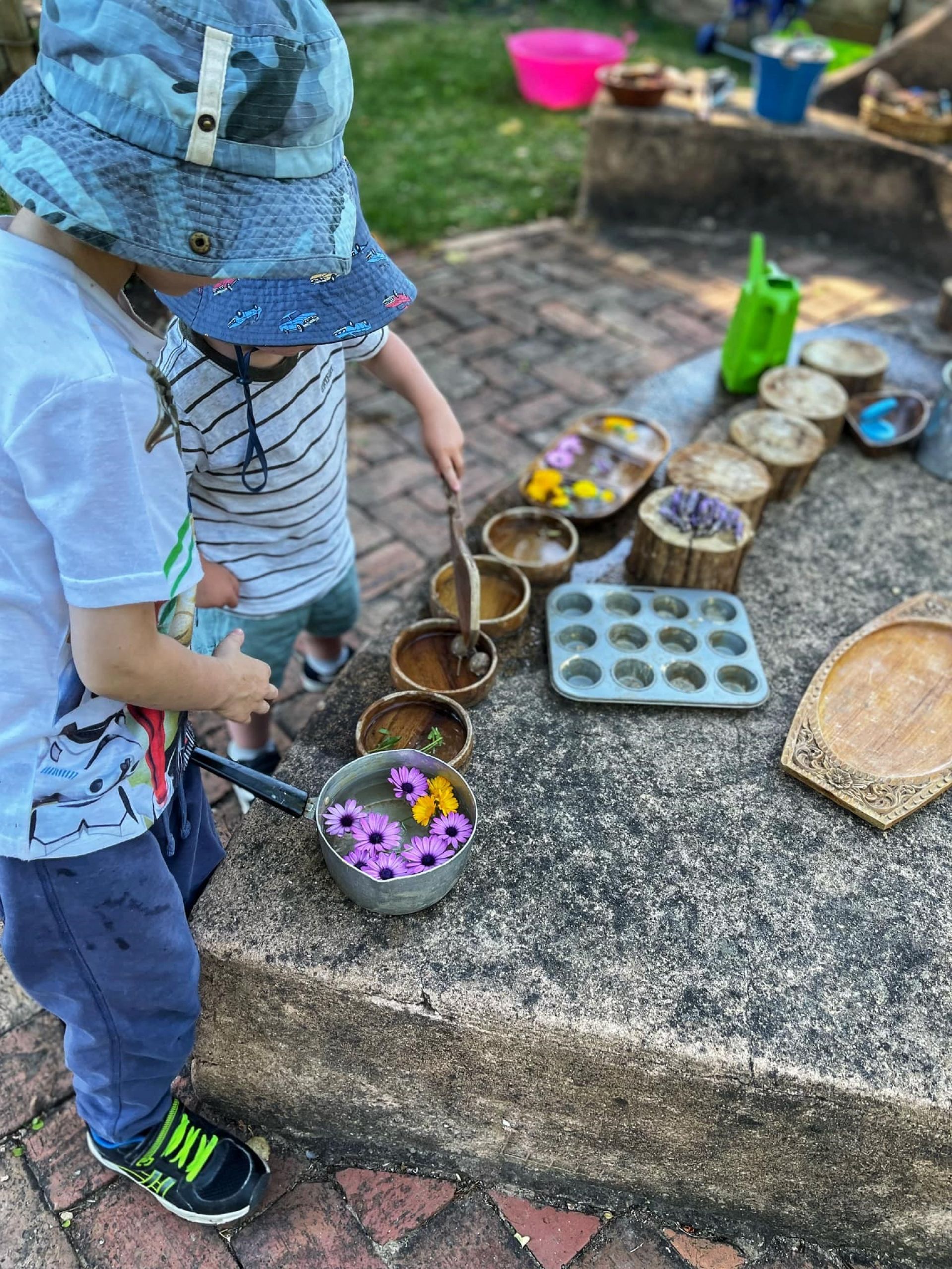 Two children doing some imaginative play with some natural objects including flowers.