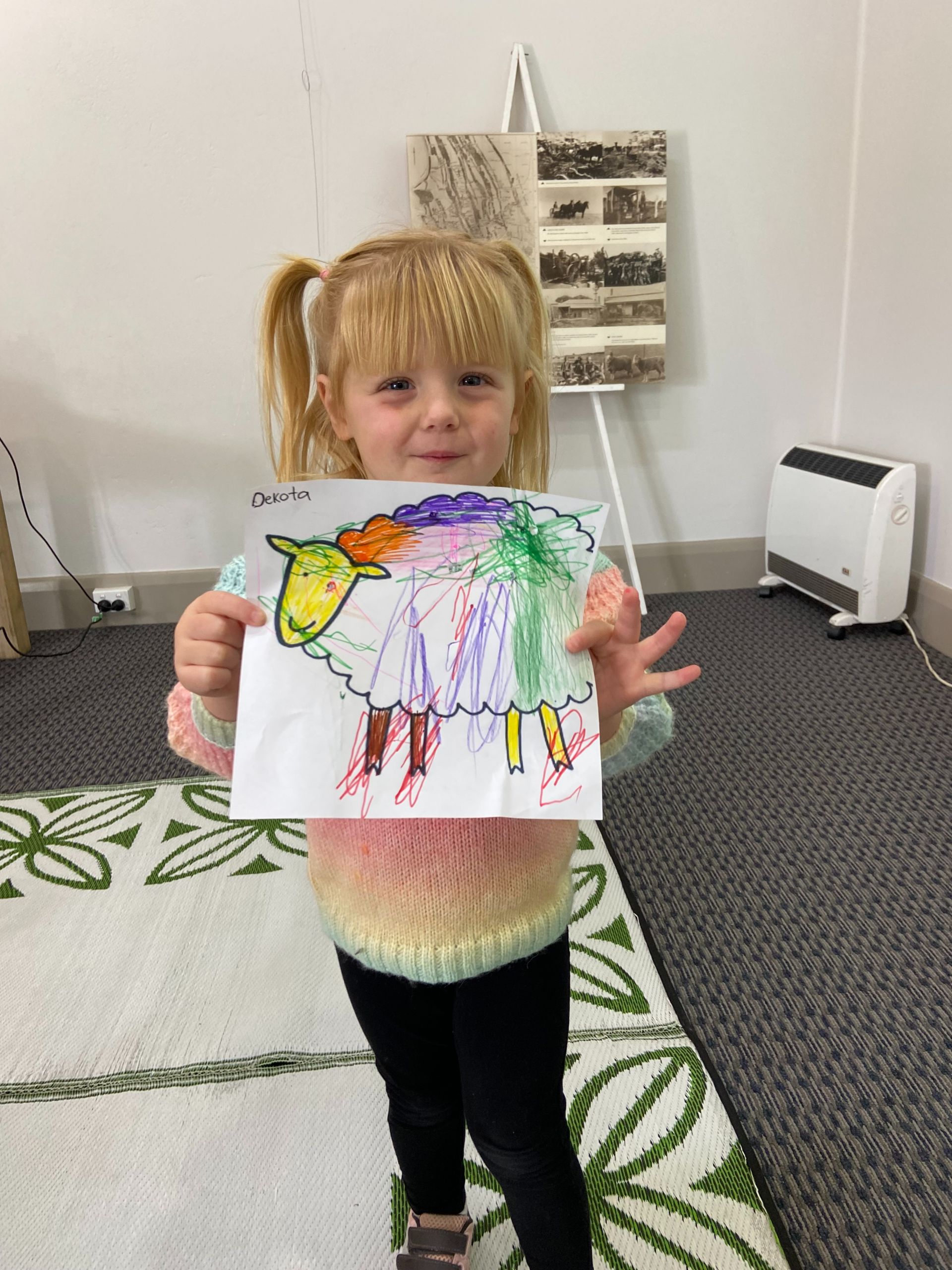 Little girl holding up a picture of a sheep she has coloured in.