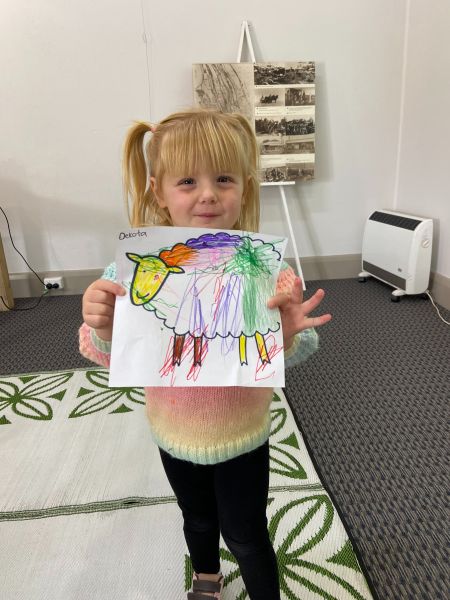 Little girl holding up a picture of a sheep she has coloured in.