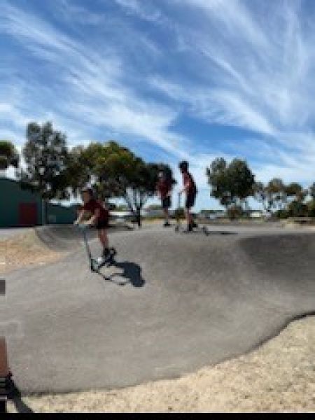 Two kids on scooters using a pump track