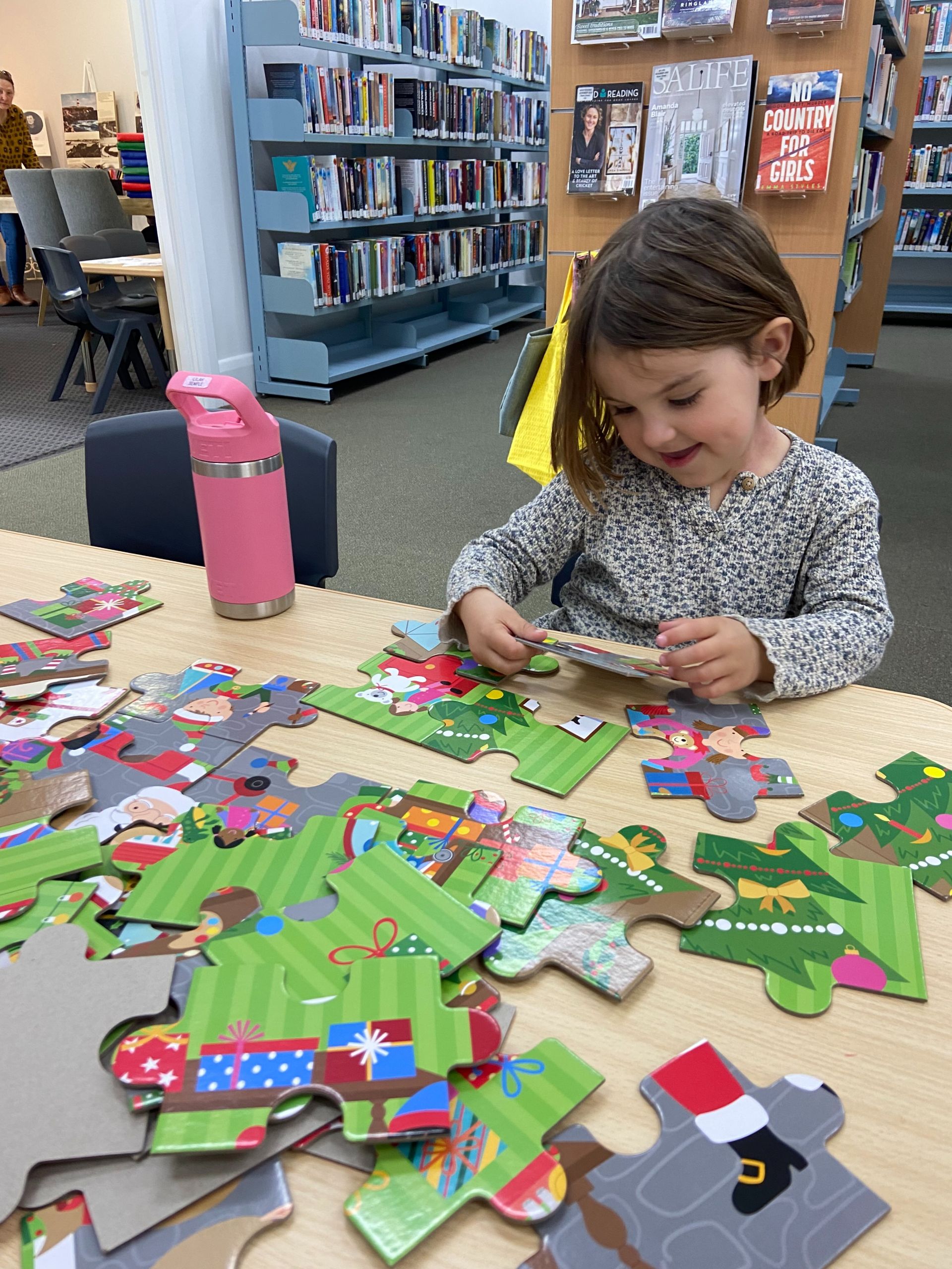 A young girl putting a large wooden puzzle together at the library