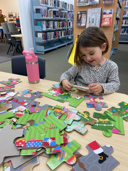 A young girl putting a large wooden puzzle together at the library
