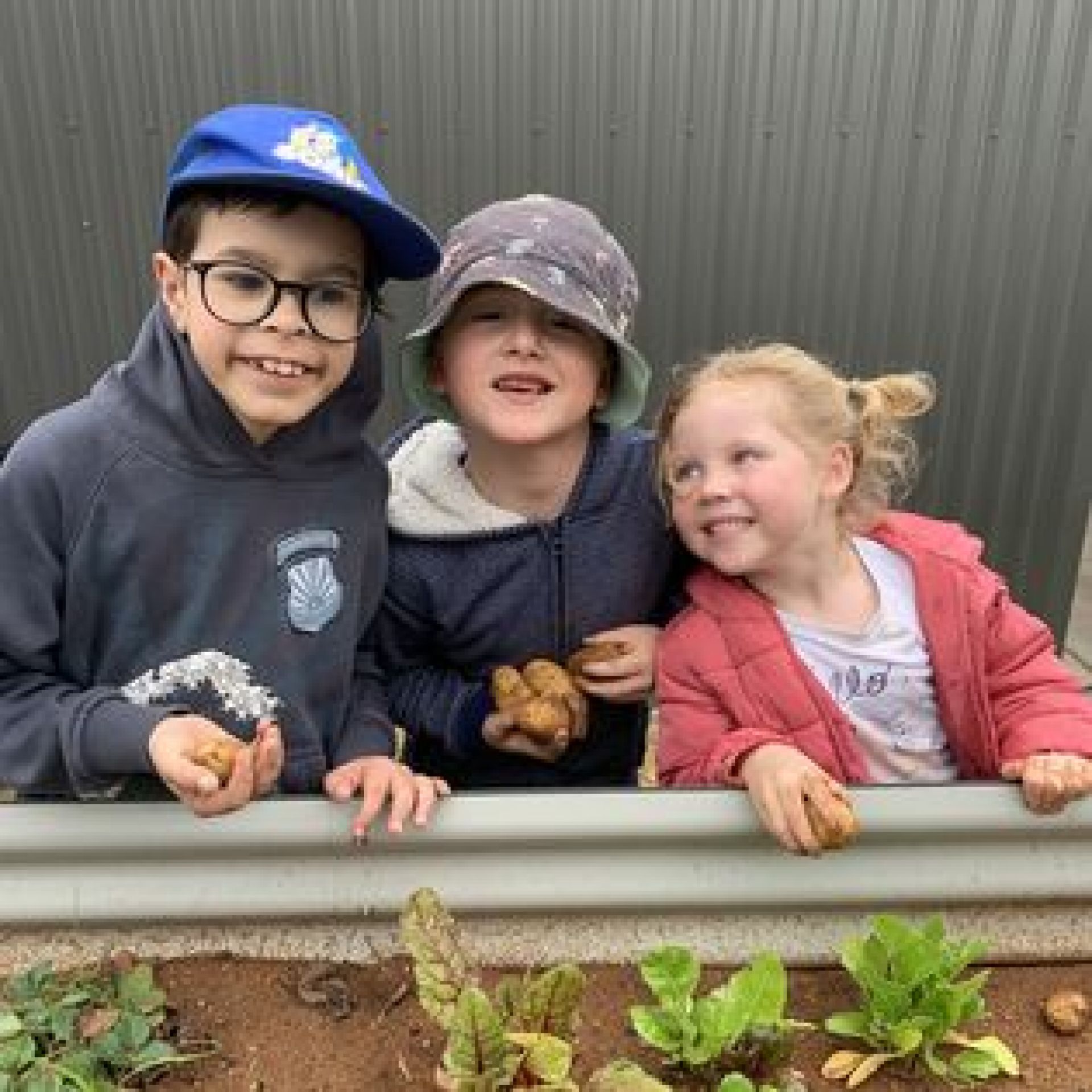 Three children standing next to a raised veggie garden