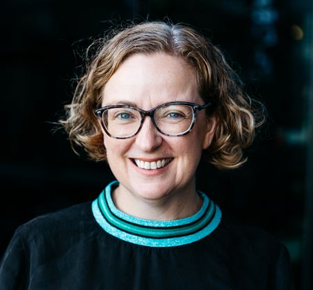 Dr Kristin Alford profile photo [Lady with short wavy light brown hair, dark framed glasses, wearing a black top with a green stripped neck line.]