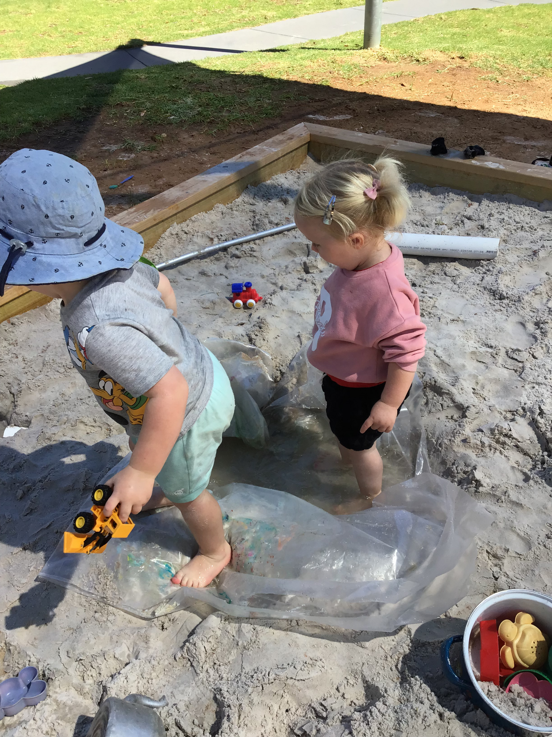 Two young children playing in the sand pit